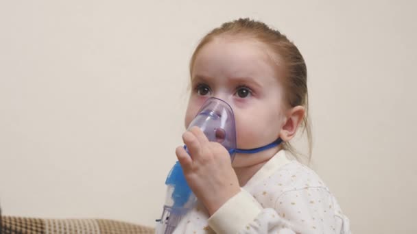 Ein niedliches Baby in Maske atmet durch einen Inhalator. Inhalationsverfahren zu Hause. Das Kind erhält eine Atemtherapie mit einem Vernebler. Behandeln Sie Ihr Baby zu Hause gegen Coronavirus. Ein kleines Kind — Stockvideo