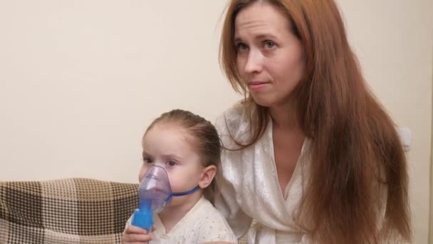 Mami inhala a una niña en una máscara con un nebulizador en casa. El niño está recibiendo terapia respiratoria con un nebulizador. Trate a su bebé por coronavirus en casa. Un niño pequeño sufre de — Vídeos de Stock