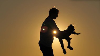 Gün batımında kızımla baba günü silueti. Kız, kollarını yanlara açmış babasının kollarında uçuyor. Kız, sevgili ailesinin kollarında gökyüzünde süzülüyor. Ayrılma