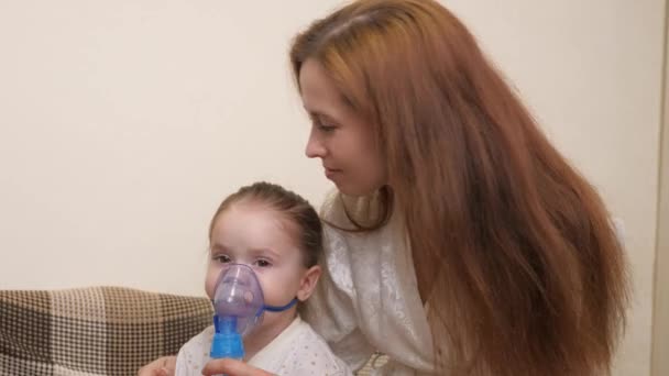 Leczenie dziecka w domu z powodu grypy i przeziębienia płuc. Dzieciak będzie wdychał nebulizator siedząc na kanapie w pokoju dziecięcym ze swoją matką. Mała dziewczynka oddycha do maski z — Wideo stockowe