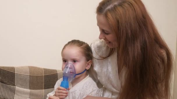 Mami inhala a una niña en una máscara con un nebulizador en casa. El niño está recibiendo terapia respiratoria con un nebulizador. Trate a su bebé por coronavirus en casa. Un niño pequeño sufre de — Vídeo de stock