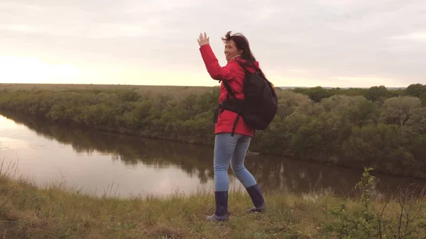 Chica feliz viajero con una mochila baila y llama a amigos. Chica alegre turista está buscando aventura. Viajes turísticos. Una forma de vida divertida. La vida es interesante y entretenida. Descanso en la naturaleza —  Fotos de Stock