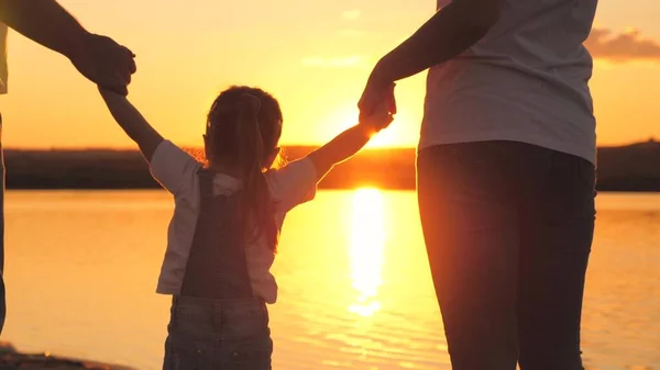 Little daughter jumping holding hands of dad and mom at sunset. Happy family life concept. A child with his parents plays together in flight. Mother and father on a walk with the kid. Spend the — Stock Photo, Image