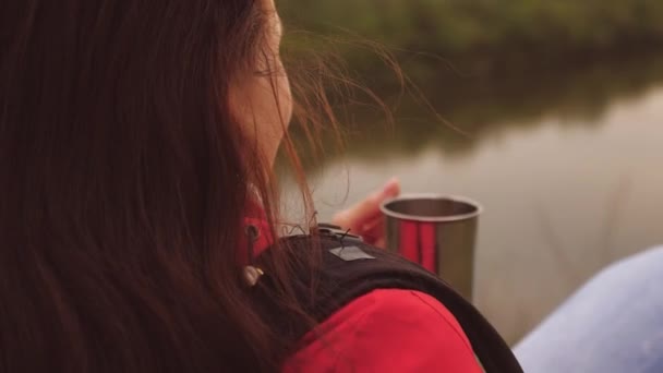 Genç bir gezgin kız dağda tek başına oturuyor ve bir kupadan sıcak çay içiyor. Hafta sonu yürüyüşüne çıkmış sırt çantalı bir kadın turist. Doğada rüzgarlı bir hava. Adam tatilde. Yalnızlık — Stok video