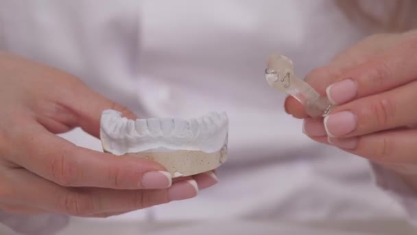 Žena ortodontistka drží v ruce talíř na opravu zubů a okluzi. Dát talíř na omítku bílé zuby. Léčba čelistí v ordinaci specializovaných lékařů. Zdravý a krásný — Stock video