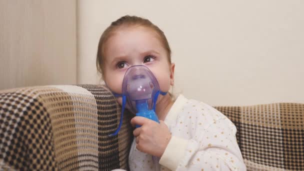 El niño está recibiendo terapia respiratoria con un nebulizador. Mami inhala a una niña en una máscara con un nebulizador en casa. Trate a su bebé por coronavirus en casa. Un niño pequeño sufre de — Vídeos de Stock