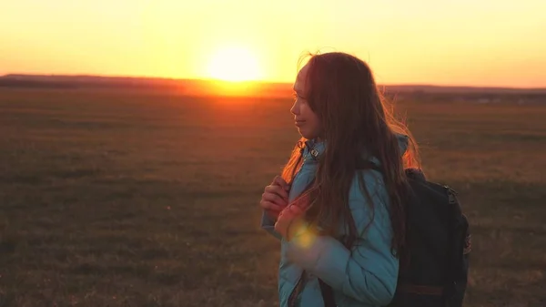 A girl traveler walks with a backpack on her back and smiles at the sunset in the sky. A teenager on a camping trip on vacation. Childhood in search of adventure from morning to dawn. Love for the