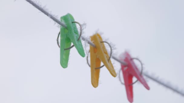 Pinzas de tela multicolores en una cuerda en escarcha cuelgan de una cuerda en el invierno afuera en la nieve — Vídeos de Stock