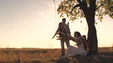 Gün batımında ailesiyle birlikte parkta oyuncak ayıyla salıncağa binen mutlu bir çocuk. Anne, kız ve baba şafakta eğleniyorlar. Mutlu aile hayatı konsepti. Sevgili annesi ve babasıyla çocuk