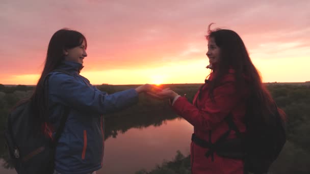 Las felices viajeras se paran en lo alto de la montaña y sostienen el sol en sus manos al atardecer en el cielo. Mujeres aventureras. Libertad de vida en un viaje de campamento al amanecer. Un buen comienzo del día en el — Vídeos de Stock