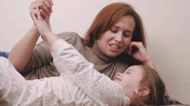 Glückliche Mutter spielt mit dem Kind auf der Couch liegend und reibt sich die Nase, Mutter lacht mit dem Kind im Kinderzimmer, Familienlebenskonzept, Eltern und kleines Mädchen gut gelaunt, Kindermädchen für — Stockvideo