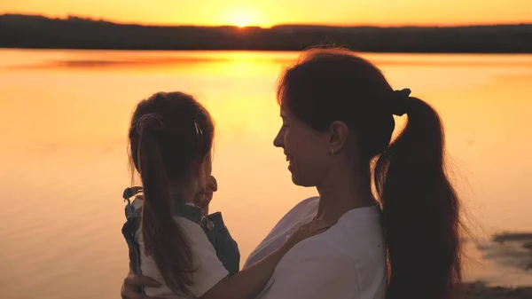 Happy mom holds a small child in her arms and plays with her noses laughing at sunset in the sky. Happy family life. Mom s day. Mother and daughter at dawn. Kid spend time with his parent. Maternal