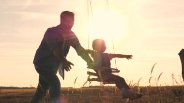 Oyuncak ayısı ve babası olan mutlu bir çocuk gün batımında parkta salıncakta salıncak sürüyor ve havada uçan uçağı çalıyor. Kızları ve babaları şafakta eğleniyorlar. Mutlu aile hayatı konsepti. Çocuk