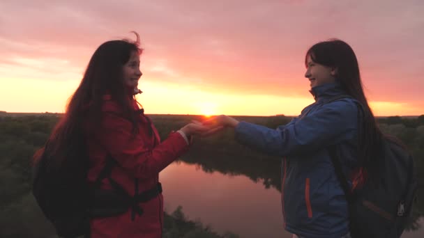 Happy female travelers stand high on the mountain and hold the sun in their hands at sunset in the sky. Women adventurers. Freedom of life on a camping trip at dawn. A good start to the day in the — Stock Video