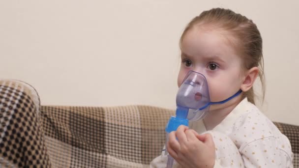 Leczenie dziecka w domu z powodu grypy i przeziębienia płuc. Dzieciak będzie wdychał nebulizator siedząc na kanapie w pokoju dziecięcym. Mała dziewczynka oddycha do maski z lekarstwem — Wideo stockowe