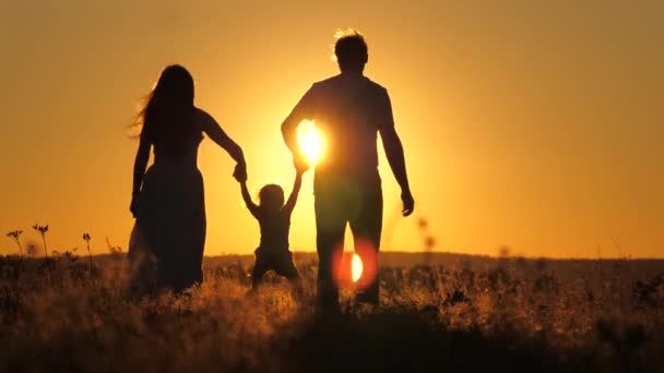 Uma criança pequena caminha com mamãe e papai em um pôr-do-sol brilhante no céu. Conheça o nascer do sol com sua família enquanto viaja. Vai caminhar com os teus pais. Criança e pais amorosos caminham no parque — Vídeo de Stock