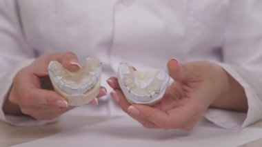 Bir kadın ortodontist elinde diş düzeltme ve tıkanıklığı için bir tabak tutuyor. Plastik beyaz dişlere plaka takmak için. Uzman bir doktorun ofisinde çene tedavisi. Sağlıklı ve güzel