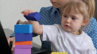 Anne kucağında küçük bir çocukla dizüstü bilgisayarda çalışıyor, çocuk renkli küplerden bir kule topluyor, bağımsız bir kadın bebeğe bakıyor, evde çalışıyor, evde oturuyor, çevrimiçi para kazanıyor.