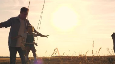 Oyuncak ayısı ve babası olan mutlu bir çocuk gün batımında parkta salıncakta salıncak sürüyor ve havada uçan uçağı çalıyor. Kızları ve babaları şafakta eğleniyorlar. Mutlu aile hayatı konsepti. Çocuk