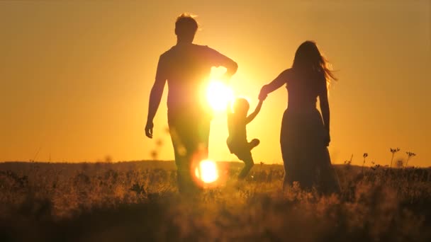 Uma criança pequena caminha com mamãe e papai em um pôr-do-sol brilhante no céu. Conheça o nascer do sol com sua família enquanto viaja. Vai caminhar com os teus pais. Criança e pais amorosos caminham no parque — Vídeo de Stock