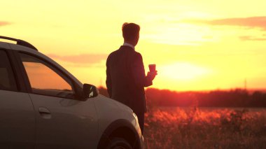 Sahte takım elbiseli bir işadamı, gün batımında kahve içer, arabanın yanında durur, direksiyonun arkasında özgürce dolaşır, konsantre olur ve geleceği düşünür, şafak vakti bir adamı.