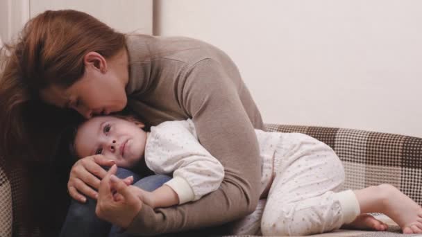 Gelukkig moeder knuffelt de baby terwijl liggend op de bank in de kinderkamer en glimlacht. Moeder en dochter liefde in familierelaties concept. Ouderlijke zorg en zorg voor het kind. Je favoriete baby wel. — Stockvideo