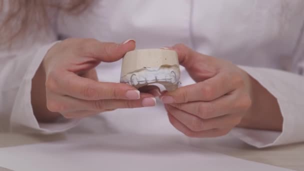 Una donna ortodontista tiene in mano una piastra per correggere denti e occlusione. Mettere il piatto sui denti bianchi intonaco. Trattamento della mandibola in uno studio medico specializzato. Un sano e bello — Video Stock