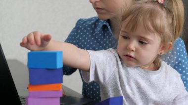 Anne kucağında küçük bir çocukla dizüstü bilgisayarda çalışıyor, çocuk renkli küplerden bir kule topluyor, bağımsız bir kadın bebeğe bakıyor, evde çalışıyor, evde oturuyor, çevrimiçi para kazanıyor.