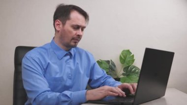 Ciddi bir adam ofiste dizüstü bilgisayarda çalışıyor, bir çalışan bilgisayarda iş yapıyor, bir serbest çalışan önemli belgeleri klavyeye yazıyor, faturalar internet üzerinden ödeniyor.