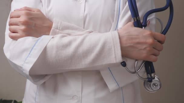 Beyaz önlüklü bir kadın doktor ellerinde steteskop, bir klinikte tedavi ve muayene tutuyor, sağlık görevlileri hastanede muayene ediyorlar. — Stok video