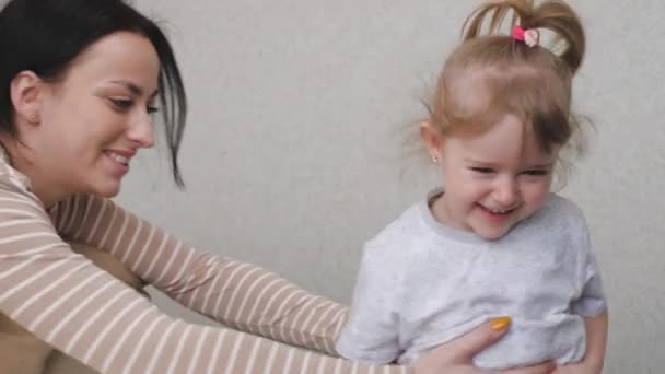 Een klein gelukkig kind en moeder spelen inhaalslag in de kinderkamer, het meisje lacht terwijl ze wegloopt van haar moeder binnen, de oppas is bezig met het kind in een entertainmentprogramma, de — Stockvideo