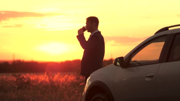 Un homme d'affaires après une dure journée de travail se tient au coucher du soleil près de la voiture et boit du café, un homme rencontre l'aube en voyage d'affaires, se repose avant un long voyage, passe la solitude à l'extérieur avec une tasse de thé chaud — Video