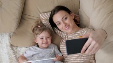 Neo anne ve bebeğinin bir yatakta babaya ya da akrabalara özçekim ya da video görüşmesi yaptığı otantik bir fotoğraf. 8K 'de çekilmiş. Teknoloji kavramı, yeni nesil, aile, bağlantı, ebeveynlik