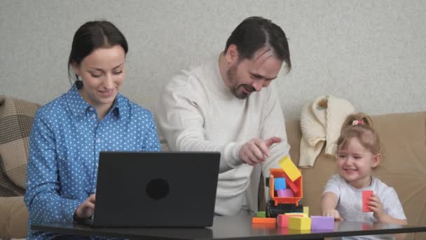 Mam is een freelancer die thuis aan de computer werkt, het kind en papa spelen met kleurrijke kubussen, de ontwikkeling van motoriek van het kind, de levensstijl van het gezin, ouders voeden een dochtertje op — Stockvideo