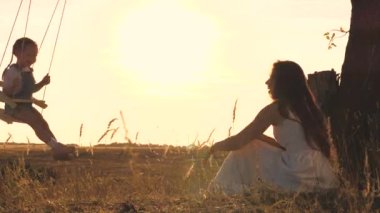 Mutlu anne küçük çocuğu salıncakta sallıyor, çocuk annesiyle oynarken uçma hissini yaşıyor, yerden göğe yükseliyor, mutlu bir aile hayatı kavramı.