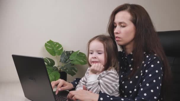 Νεαρή επιχειρηματίας εργάζεται σε ένα γραφείο στο σπίτι με ένα φορητό υπολογιστή με ένα παιδί στην αγκαλιά της, ένας ελεύθερος επαγγελματίας σε έναν υπολογιστή σε απομακρυσμένη εργασία σε καραντίνα με ένα παιδί, η έννοια της ευτυχούς οικογένειας, ένα παιδί — Αρχείο Βίντεο