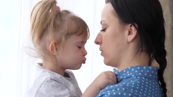 Une petite fille embrasse sa mère bien-aimée, maman tient l'enfant dans ses bras et ses câlins, le concept d'une vie familiale heureuse, la nounou calme l'enfant, le parent est à côté de l'enfant ensemble, 4K, gros plan — Video