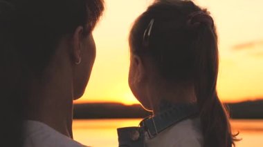 Mutlu anne ve küçük kız gün batımında gökyüzünde kucaklaşıp gülümsüyor, mutlu aile kavramı, anne ve çocuk şafakta buluşuyor, macera ve açık havada oyunlar oynuyor, ebeveynler sevgili çocukla tatil yapıyor.