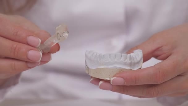 A woman orthodontist holds in her hand a plate for correcting teeth and occlusion. To put the plate on the plaster white teeth. Jaw treatment in a specialist doctors office. A healthy and beautiful — Stock Video