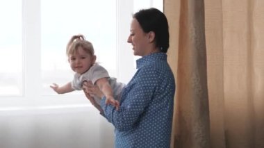 Bir kız annesinin kollarında uçuyor, çocuklu bir ebeveyn uçağı çalıyor ve gülüyor, bebek için bir eğlence programı, havada süzülüyor, mutlu bir aile hayatı kavramı, bir kadın çalışıyor