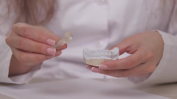 Kobieta ortodonta trzyma w ręku talerz do korekcji zębów i niedrożności. Położyć talerz na gipsowych białych zębach. Leczenie szczęk w gabinecie lekarzy specjalistów. Zdrowa i piękna — Wideo stockowe