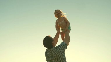 Mutlu baba güneşin parıltısıyla bir çocuğu gökyüzüne fırlatır, çocuk bir uçak gibi yükseğe uçar ve güler, küçük kız spa ile açık havada oynar, mutlu aile kavramı