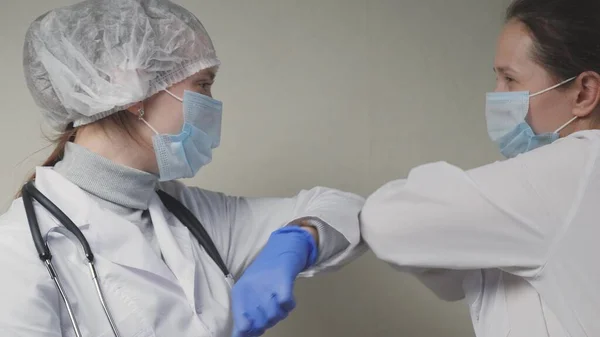 Женщины-врачи приветствуют друг друга локтями, доктор надевает защитные голубые перчатки на руки, защиту от вируса при предотвращении попадания в дыхательные пути легких — стоковое фото