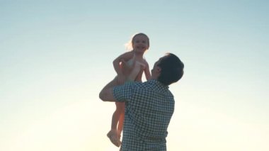 Mutlu baba güneşin parıltısıyla bir çocuğu gökyüzüne fırlatır, çocuk bir uçak gibi yükseğe uçar ve güler, küçük kız spa ile açık havada oynar, mutlu aile kavramı