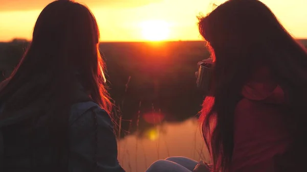 Las mujeres viajeras disfrutan de una hermosa puesta de sol con tazas de una bebida caliente, beben café vigorizante con una mañana cálida al amanecer, se calientan y sacian su sed de café en el resplandor del sol, una caminata —  Fotos de Stock