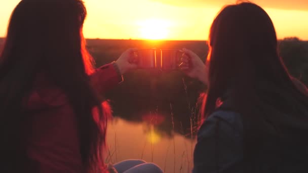 Weibliche Reisende sitzen bei Sonnenuntergang hoch oben auf einem Berg am Fluss und trinken Tee aus einem Becher. Zelten Sie am Wochenende mit einem Freund. Touristische Erkundung der Natur. Sich vom Alltag befreien — Stockvideo