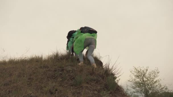 Een volwassen meisje beklimt een berg in de regengebieden met rugzakken, de vrouwelijke reizigers hebben een gezonde dag van rust samen, 4K, buitenleven, teamwork, een kampeertocht van mensen met rugzakken, langzame — Stockvideo