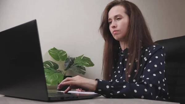 Una mujer de negocios trabaja en una computadora en la oficina, un freelancer escribe texto en el teclado, en línea en un programa de forma remota, Internet para la transferencia de datos, una chica llena y mantiene importante — Foto de Stock