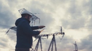Elektrik hatlarının yakınında tabletle çalışan kıdemli elektrik mühendisi. Kıdemli elektrik mühendisi elektrik enerjisi dağıtır. Bir tabletle elektrik enerjisiyle çalışan iş adamı elektrikçi.