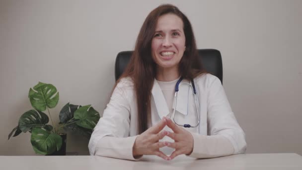 Žena doktor vybuchne smíchem, kardiolog v kanceláři sedí v křesle u stolu, mladá dívka pediatr v bílém plášti, obchodní lékařské služby — Stock video